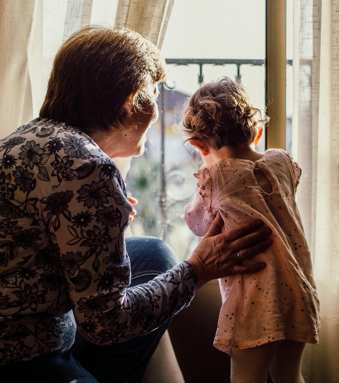 grandma-and-grand-daughter Grand mother and granddaughter looking out a home window, viewed from behind