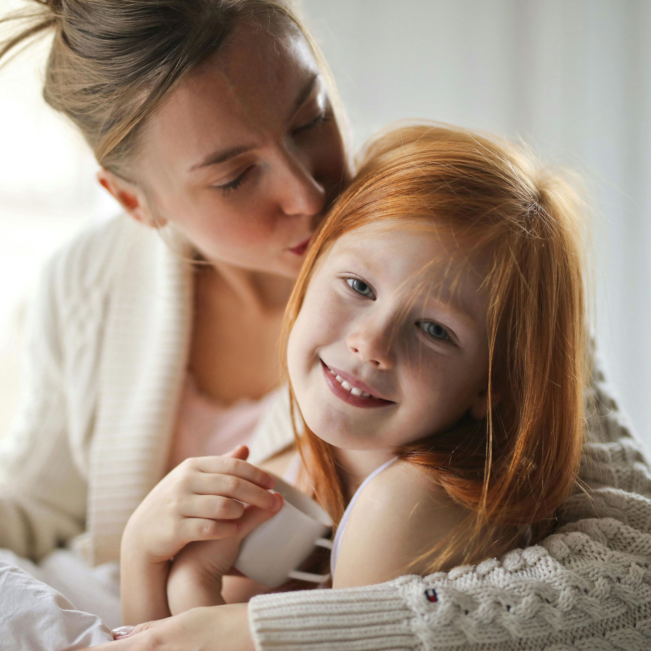 Blonde-haired Mother and red-haired daughter cuddled up 