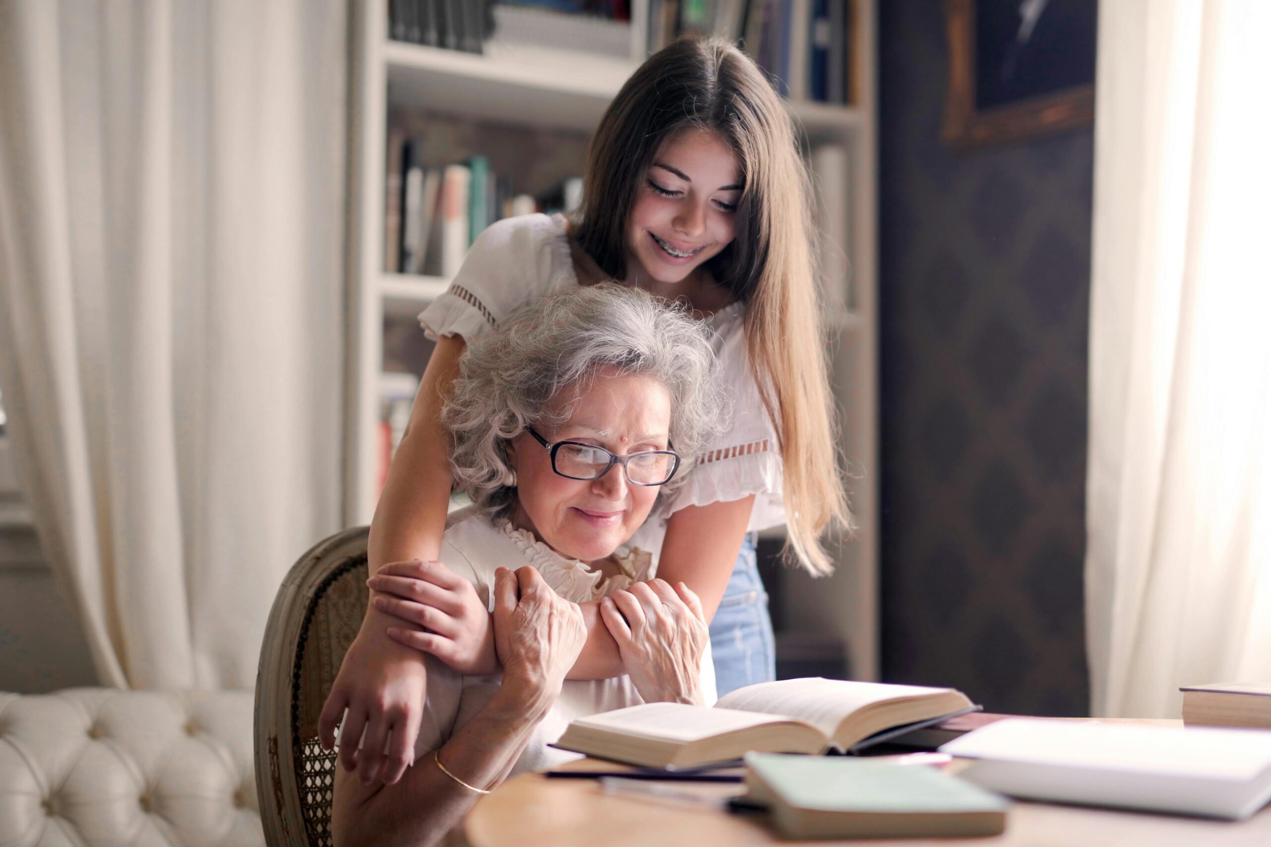 grandma-and-granddaughter Granddaughter standing behind grandmother reading a book, both smiling